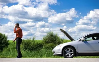 image3-p-500 A man on a road talking on his phone while a white car with an open hood is stopped nearby